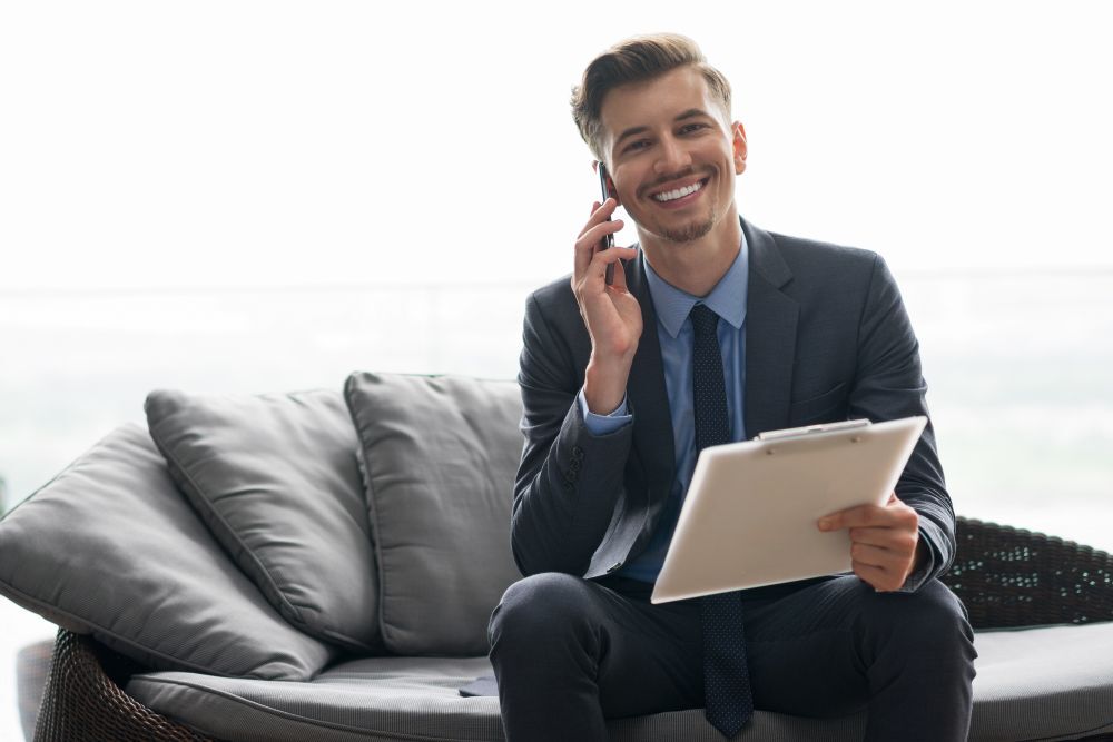 Administrador de fincas profesional con traje sonriendo mientras resuelve gestiones de propiedades por teléfono de forma eficiente.