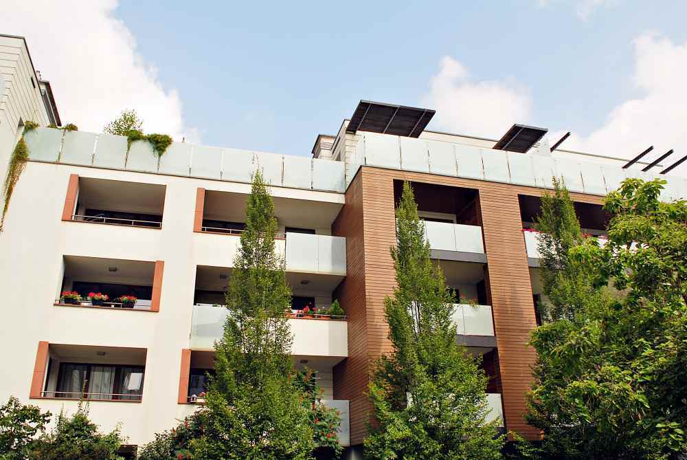 Vista exterior de un complejo residencial moderno y luminoso con balcones de cristal y zonas ajardinadas bajo un cielo soleado.